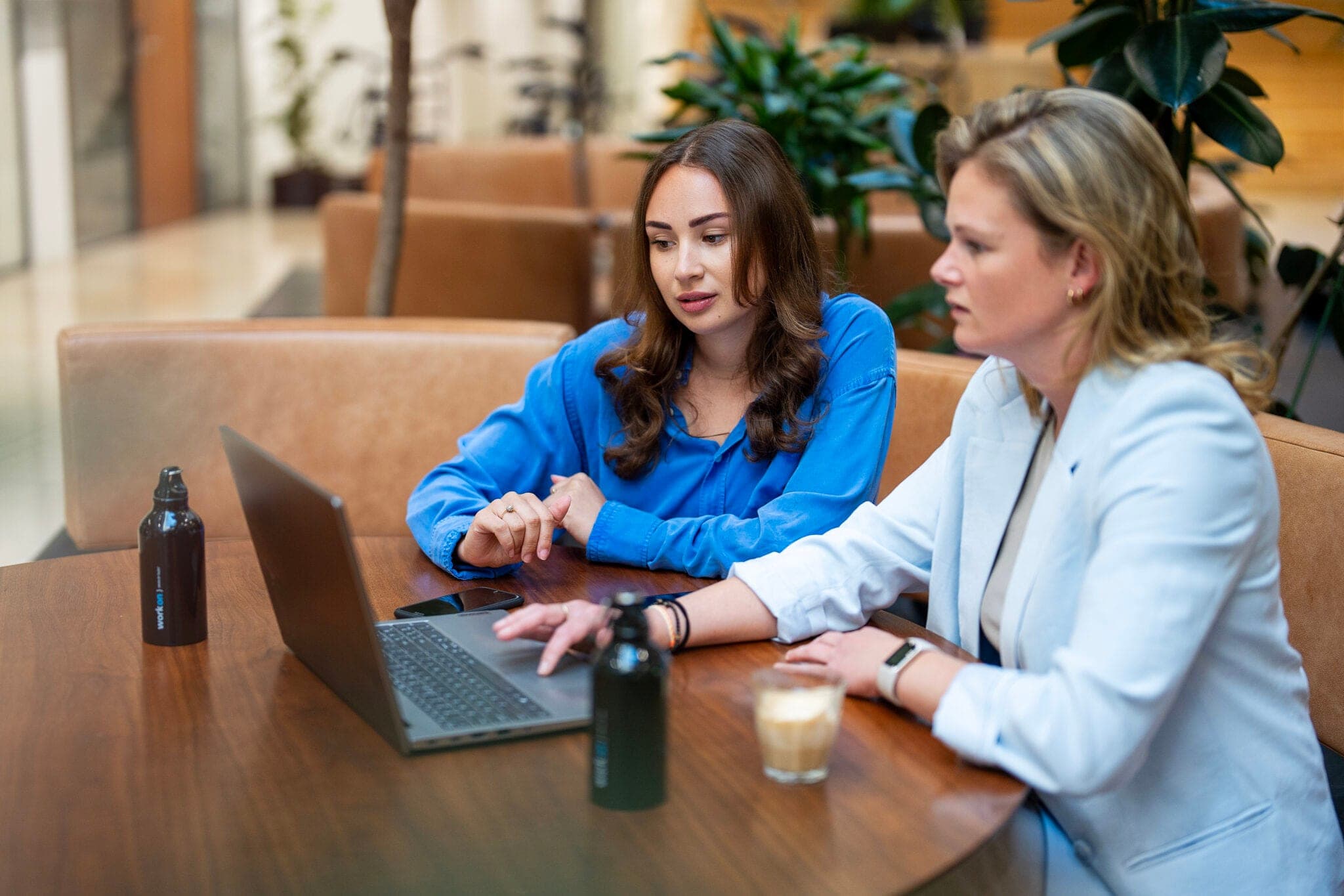 Twee vrouwen overleggen samen achter een laptop aan een ronde tafel.