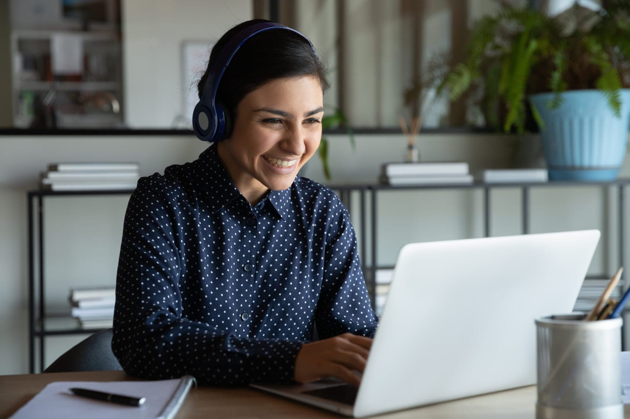 Medewerker van een zorgverzekeraar helpt lachend een klant via haar headset, achter haar laptop.